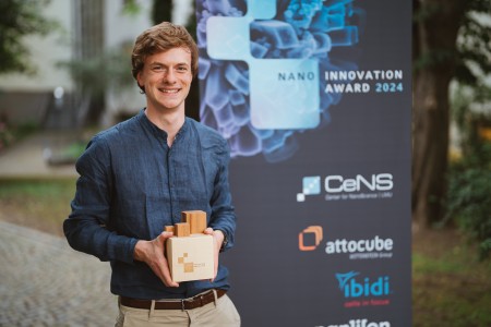 Researcher smiling and holing a Nano Innovation Award made of wood. 