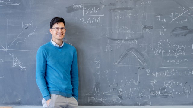 Professor standing in front of a black board filled with formulas.